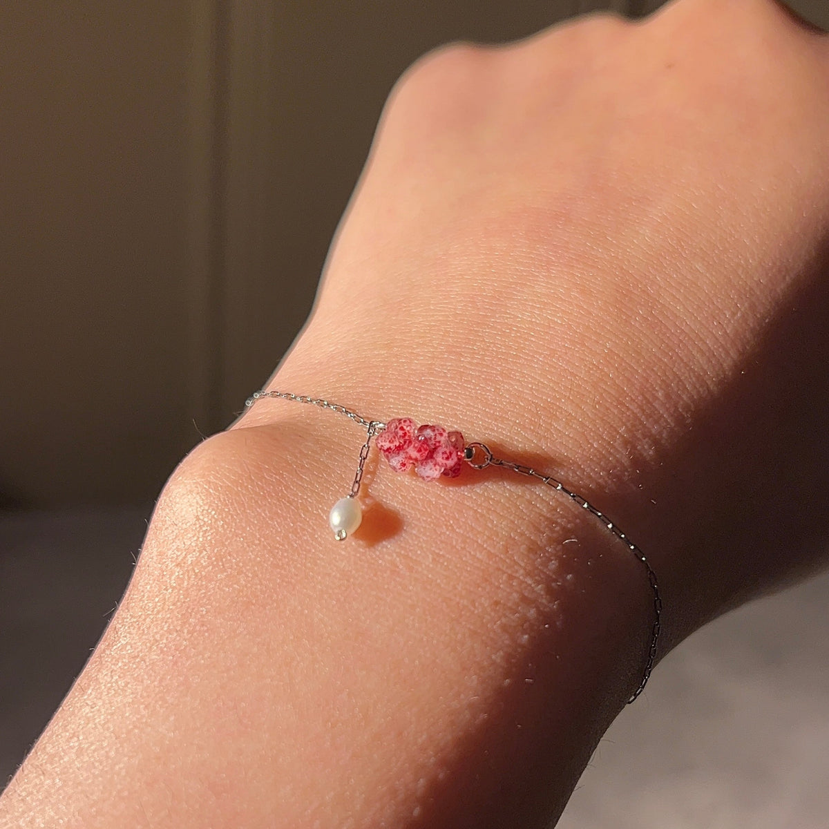 Delicate bracelet with pink rose details and a dangling pearl-like accent on a wrist